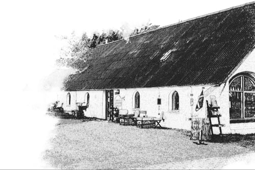 Sorte-hvide illustration af en hyggelig ældre landsbykirke med udendørs borde og stole foran.