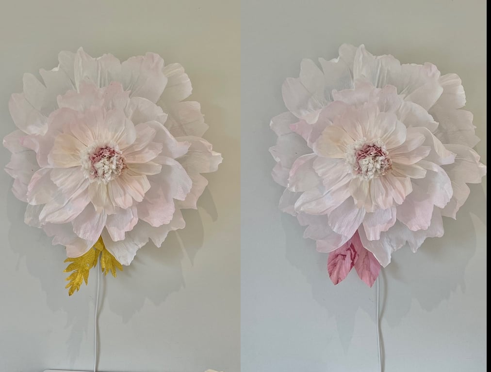 To store kunstige blomster i lyse pastelfarver, den ene med gule blade, den anden med lyserøde, begge monteret på væg med ledninger.