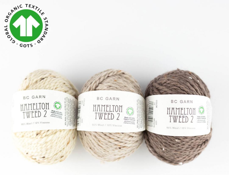 Tre nøgler af BC Garn Hamilton Tweed 2 garn i forskellige nuancer af beige og brun med Global Organic Textile Standard (GOTS) mærkat øverst til venstre.