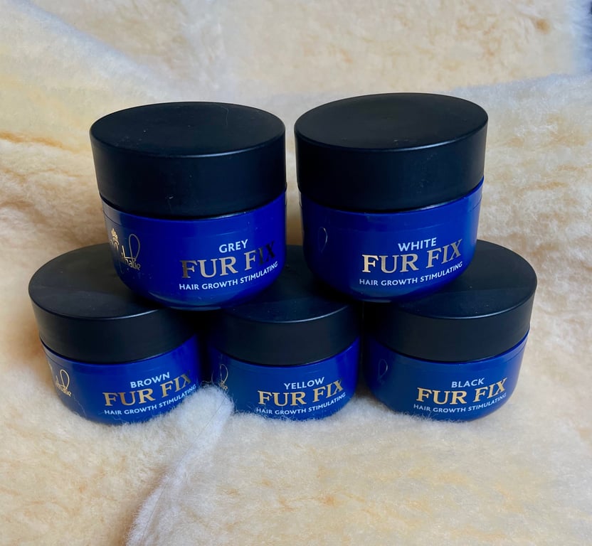 Blå krukker med sorte låg, mærket "Fur Fix" til hårvækststimulerende behandling i farverne grey, white, brown, yellow og black, placeret på en lys pels.