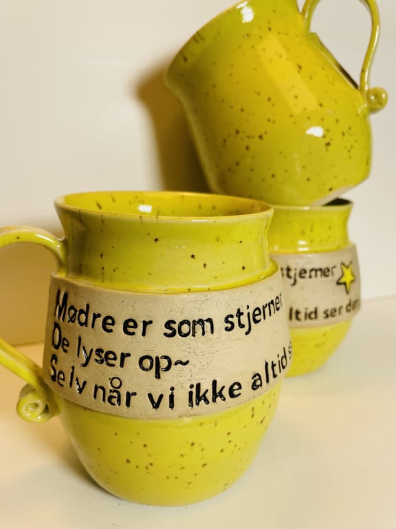To gule keramik krus med sort dansk tekst og stjerneillustration, hvor teksten hylder mødres betydning som stjerner, der lyser op selv når de ikke altid ses.