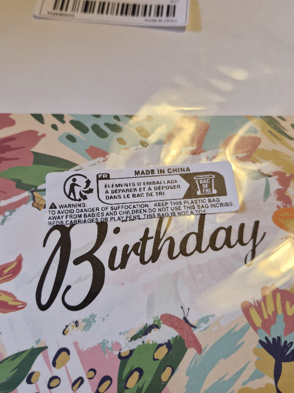Et billede af en plastikpose med en advarselsetiket på engelsk og fransk. Teksten "Birthday" er delvist synlig under plastikken, omgivet af farverige blomsterillustrationer.