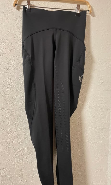 Sort rideleggings med høj talje, hængende på en bøjle mod en hvid væg.