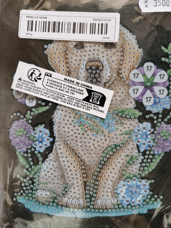 Pakke med diamantmaleri af en sød hund blandt lilla og blå blomster, dækket af advarsels- og prisetiketter.