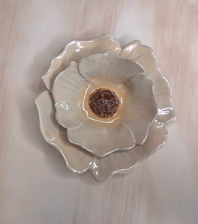 Keramisk blomsterfigur med glaserede, beige og brunlige farver lagt på lyst træbord.