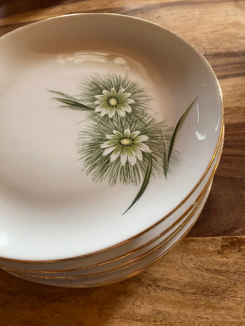 Stabel af hvide porcelænsskilte med grønne blomster- og bladmotiver og guldkant, placeret på et træbord. (2)