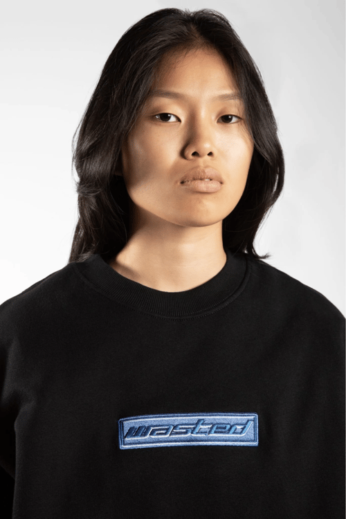 Portræt af ung kvinde med mørkt hår iført sort sweatshirt med blå label med teksten "wasted". (2)