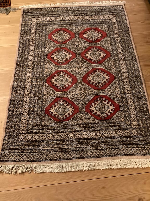 Tæppe med mønster af røde oktagoner og detaljer i sort og hvidt, lagt på lyst trægulv. (2)