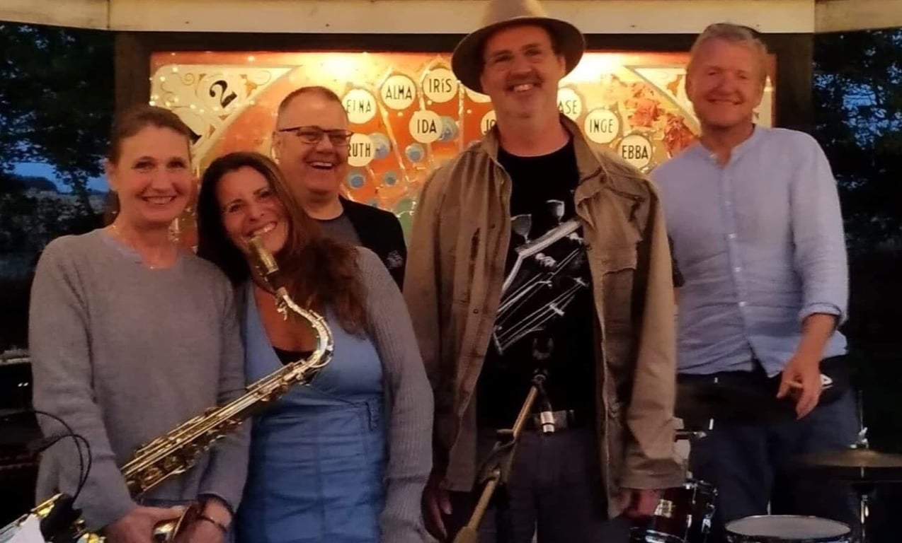 Foto af fem glade mennesker samlet, hvor en kvinde holder en saxofon.