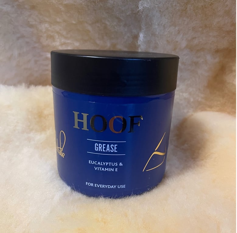 Blå beholder med sort låg mærket "HOOF GREASE" med eucalyptus og vitamin E, placeret på blødt, lyst uldmateriale.