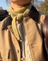 Nærbillede af en person iført en lysebrunt jakke, en beige cardigan og en gulstrikket halstørklæde. (3)