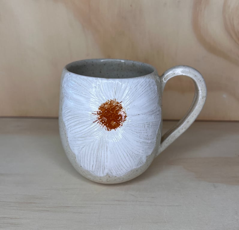 Keramikkrus med håndmalet hvid blomst med orange midte på beige baggrund.