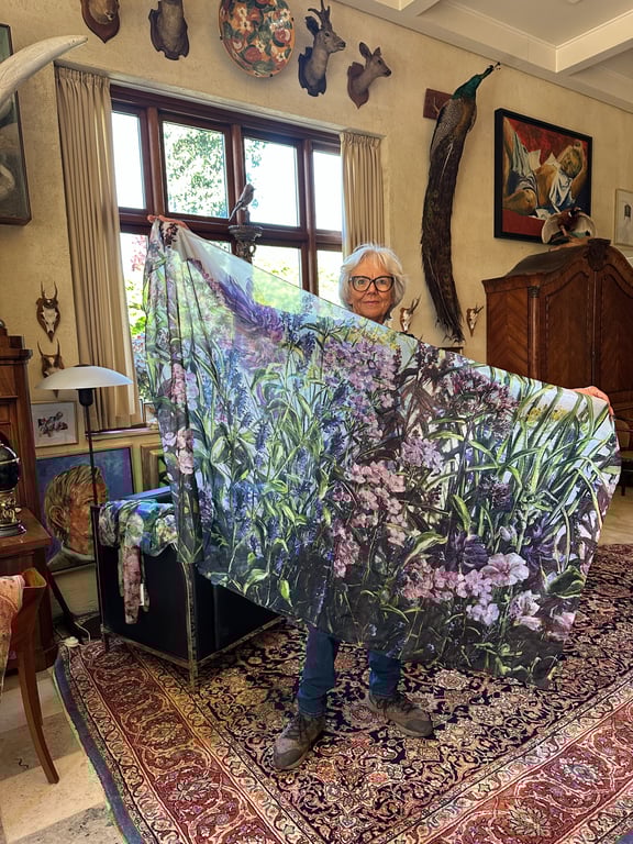 Ældre kvinde i stue med jagttrofæer, der holder et stort tørklæde med blomsterprint.