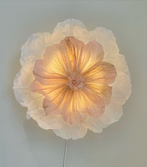 Lyskilde formet som en stor, blomst med lag af transparente, bløde kronblade i hvide og lyserøde nuancer, der udsender varmt lys. (1)
