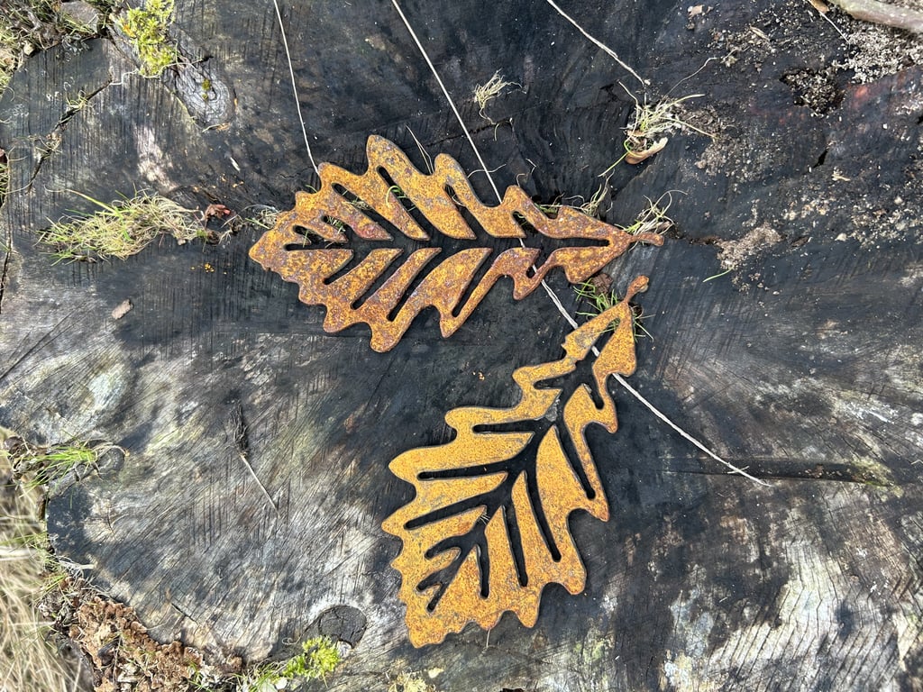 To rustne metalblade formet som egeblade ligger på en mørk træstamme med mos omkring.