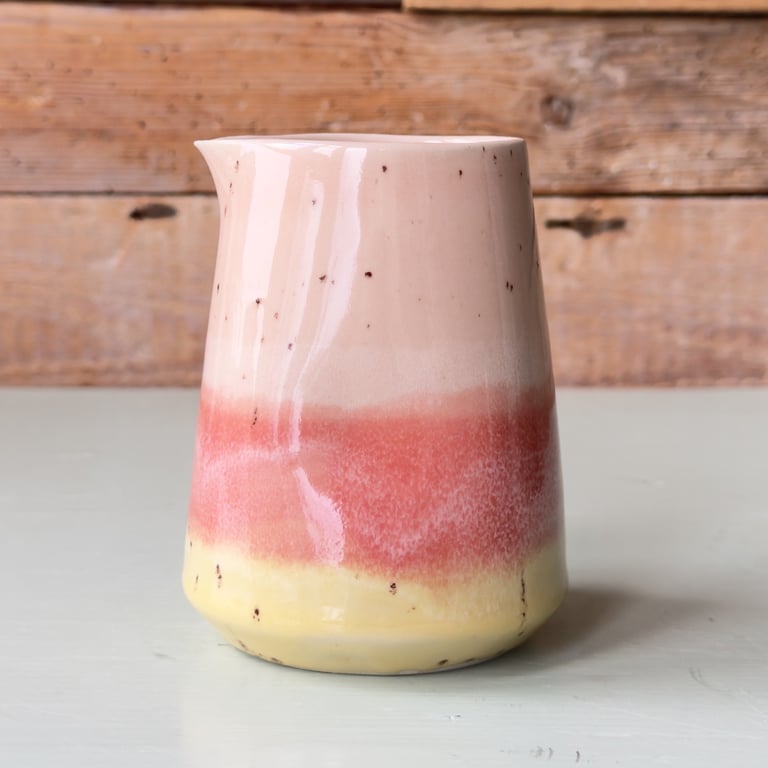 Keramisk kande med tre farvezoner i beige, rød og gul, placeret på en lys overflade med træbaggrund.