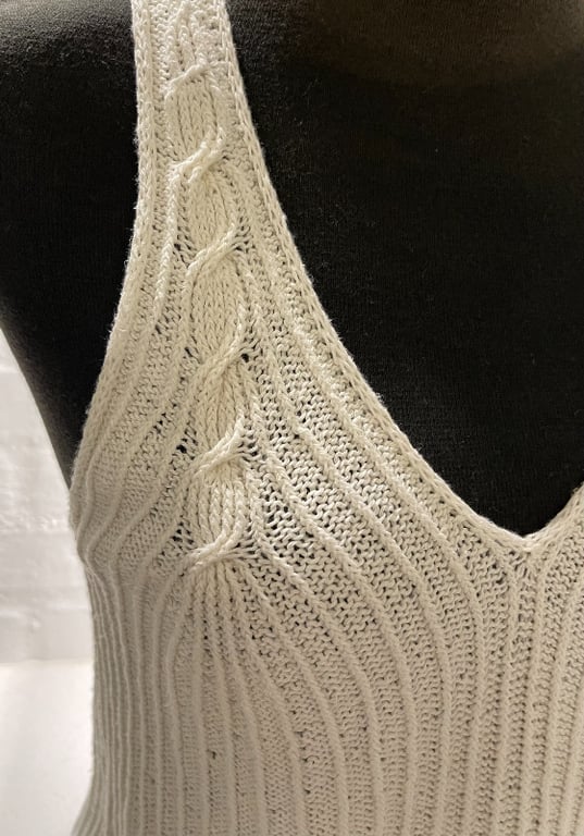 Nærbillede af en strikket, hvid top med kabelstrikdetaljer på en sort mannequin.