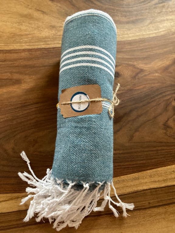 Blåt og hvidt stribet tekstil med frynser, rullet sammen og bundet med snor på træbord. (2)