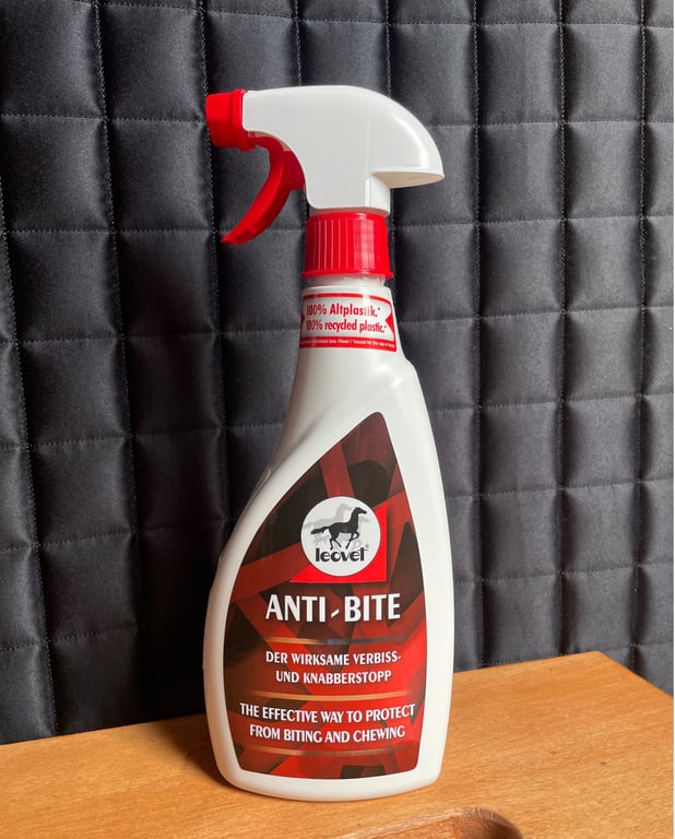 Sprayflaske med anti-bid middel fra Leovet på et lyst træbord foran en sort quiltet baggrund.