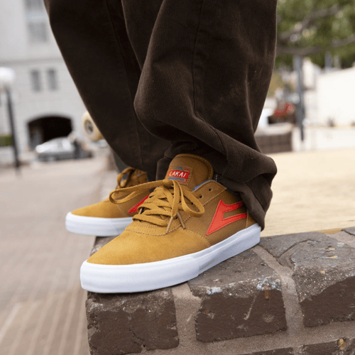Nærbillede af fødder iført sennepsgule og røde sneakers, stående på en murstenskant. (1)