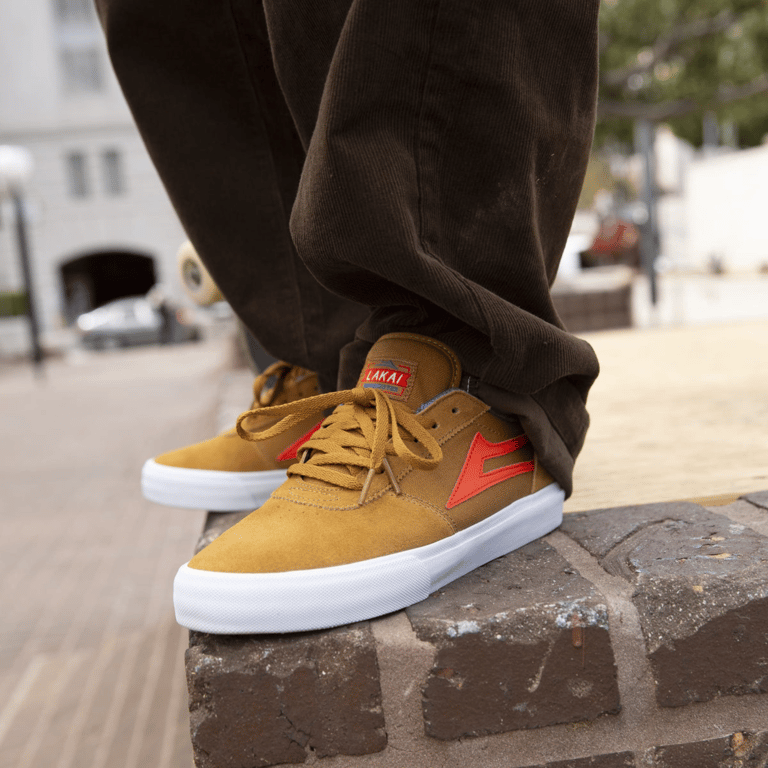 Nærbillede af fødder iført sennepsgule og røde sneakers, stående på en murstenskant.