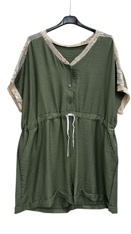 Kortærmet grøn jumpsuit med beige netdetaljer ved ærmer og halsudskæring, knapper foran og hvid snor i taljen, hængende på sort bøjle.