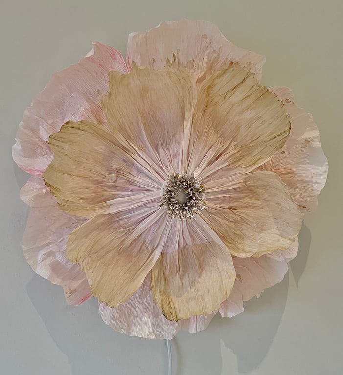 Stor, cremefarvet og rosa kunstig blomst med detaljerede kronblade mod en lys baggrund.