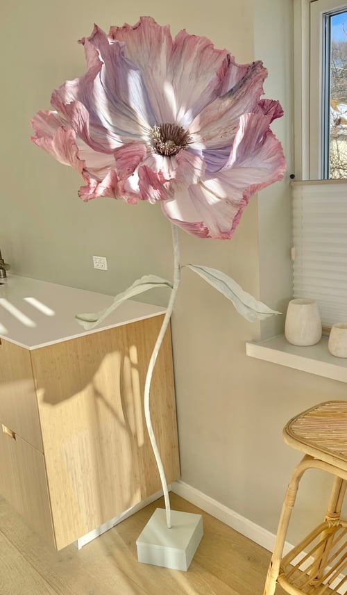 Stor kunstig blomst i lyserøde og hvide nuancer, placeret i et lyst rum med træmøbler og et vindue i baggrunden. (1)