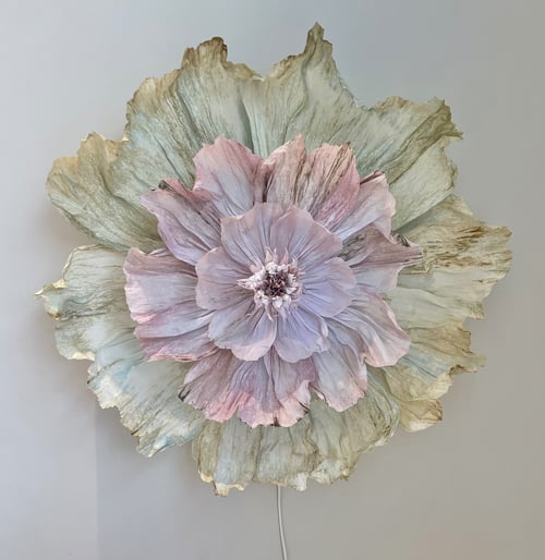Stor dekoration formet som en blomster med lag på lag af pastelfarvede og grønne krøllede blade mod en lys væg. (1)