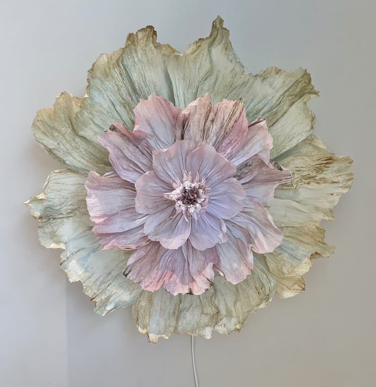 Stor dekoration formet som en blomster med lag på lag af pastelfarvede og grønne krøllede blade mod en lys væg.