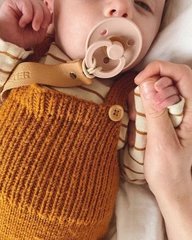 Baby med sut iført brun/orange strikket hakelap-holder og smørfarvet body med striber, der holder en voksen hånd. (2)
