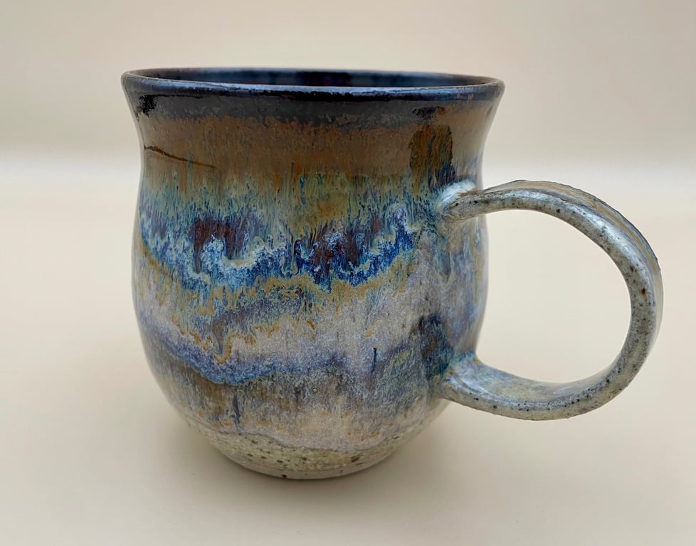 Keramisk krus med unikt blåt, brunt og beige glasurmønster og stort håndtag set fra siden.