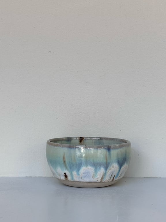 Keramisk skål med blå, grønne og brune nuancer mod hvid væg.