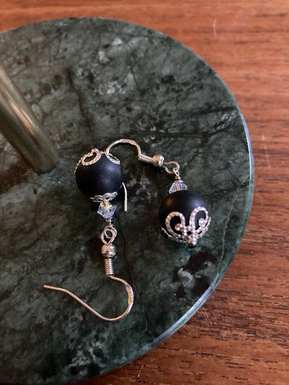 To sorte perleøreringe med sølvdetaljer og små krystaller, lagt på en grøn marmorplade. (2)