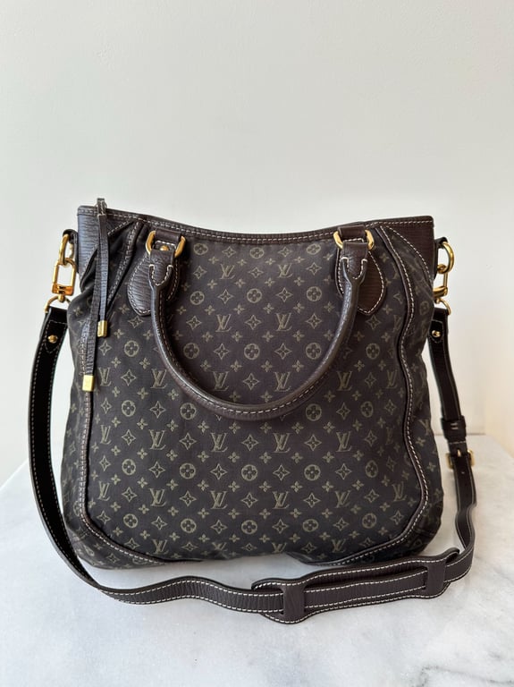 Brun Louis Vuitton håndtaske med monogrammønster og både kort håndtag og lang justerbar skulderrem, placeret på en lys flade mod en hvid væg.