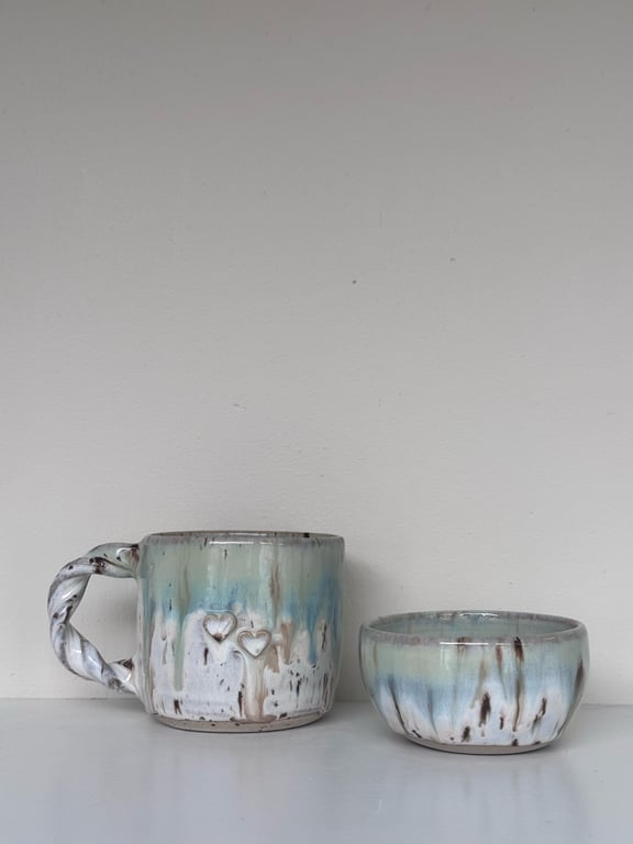 Keramikkrus og skål med glasur i blå, hvid og brunlige nuancer, kruset har håndtag med snoet design og to små hjerter som dekoration.