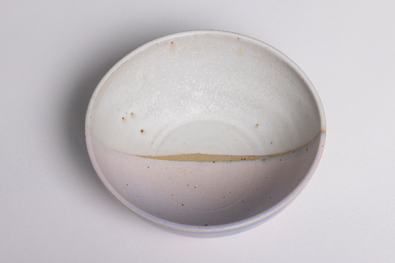 Keramisk skål med glaseret hvid og lyserød overflade samt små brune pletter.