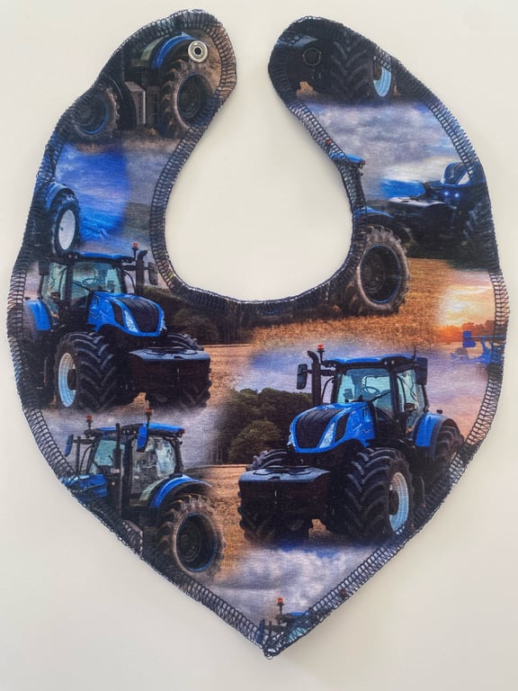 Babysavletøj i form af et hjerte, dekoreret med print af blå traktorer på en mark ved solnedgang.