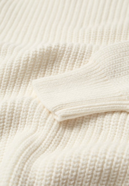 Nærbillede af en cremefarvet strikket sweater med ribstrik på ærmet.