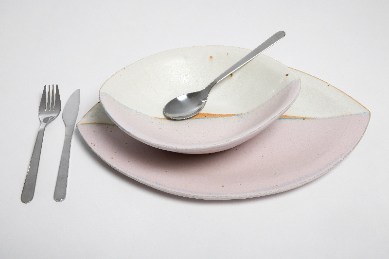 Et keramisk tallerken- og skålarrangement med en ske og kniv, skabt i en blid pastel- og naturlig tone på en hvid baggrund.