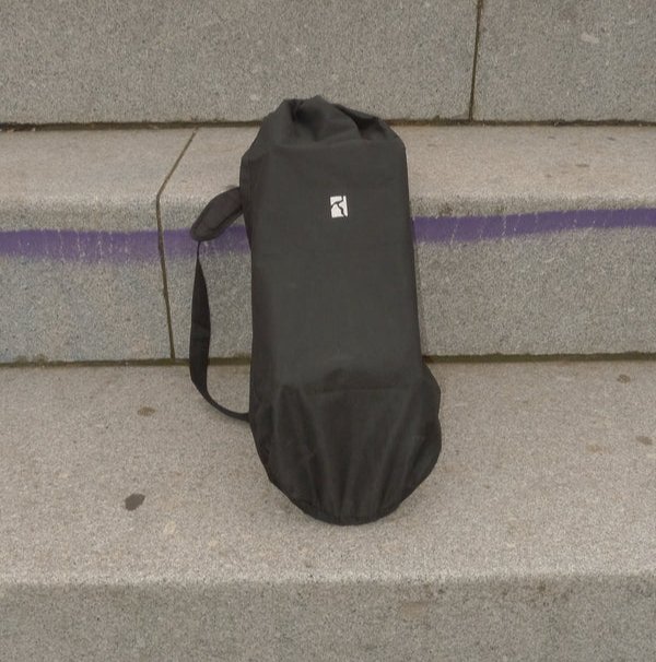 Sort opbevaringspose med skulderrem, placeret på en betontrappe med en lilla streg bagved.