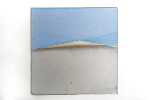 En keramisk flise med et minimalistisk maleri af en bjergkæde under en blå himmel.