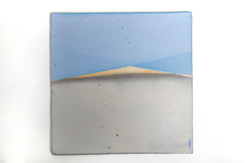 En keramisk flise med et minimalistisk maleri af en bjergkæde under en blå himmel.
