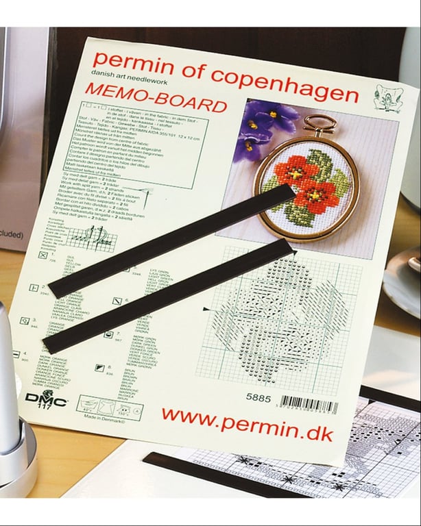 Billede af et Permin of Copenhagen memo-board med broderiopskrift og to sorte magneter lagt ovenpå.