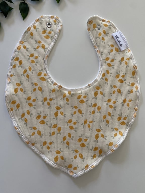 Babysavlesmæk i hvid med gul-orange og lysegrå bladmønster, syet med kantbånd og trykknapper i toppen.