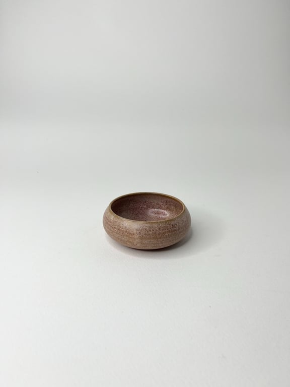 Lille rund skål i keramisk materiale med en lys brun og rosa farvetone, placeret på en hvid baggrund.