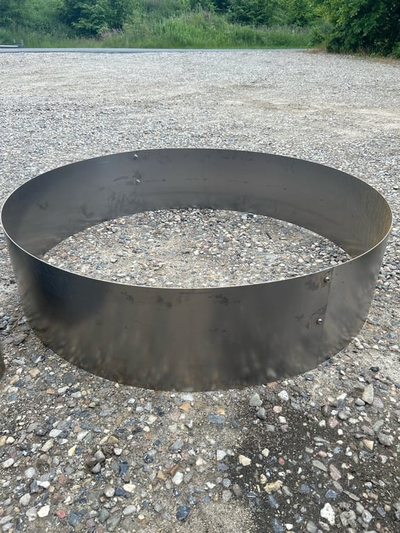 Metalring placeret på grusbelagt jord med græs og træer i baggrunden.