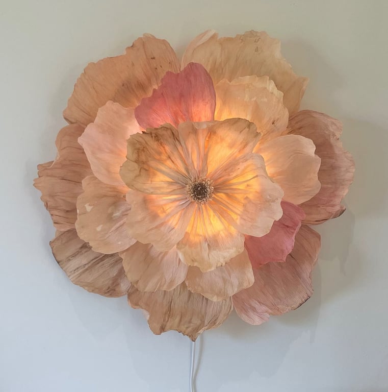 Lysende vægdekoration formet som en stor, blomst med lyserøde og beige kronblade.