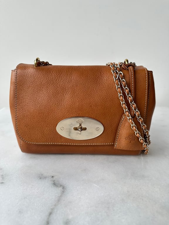 Brun lædertaske med guldfarvet kæderem og metalspænde foran, placeret på en lysegrå marmorflade.