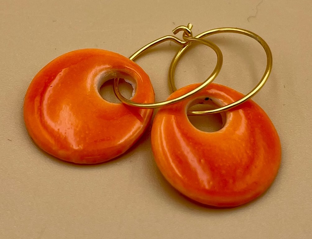 Orange keramiske øreringe med guldbøjle mod beige baggrund.